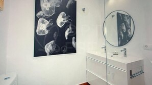 Un baño con un lavabo blanco, un espejo y una obra de arte en la pared de medusas.