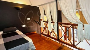 Un dormitorio con cama, suelo de madera, balcón con barandilla y vistas al exterior.