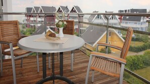 A balcony with a round table and two wooden chairs, overlooking a residential area with houses. - Ferienwohnung im Ferienpark Mueritz (Rechlin)