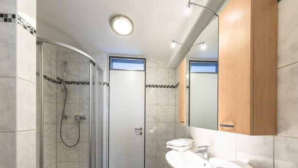 Un baño moderno con ducha envuelta en vidrio, tocador con espejo y suelo de baldosas.