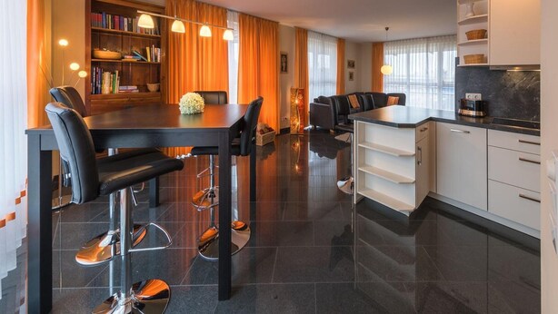 A modern kitchen with a dining area, featuring a black dining table, bar stools, and a built-in bookshelf. - Ferienwohnung im Ferienpark Mueritz (Rechlin)