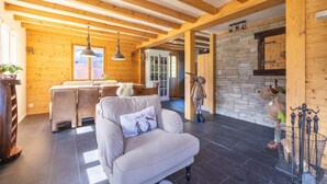 A spacious living area with a high ceiling, wooden beams, a stone wall, and a cozy seating area with a sofa and a fireplace. - Chalet Verrel Near Aletsch Ski Gondolas (Fiesch)