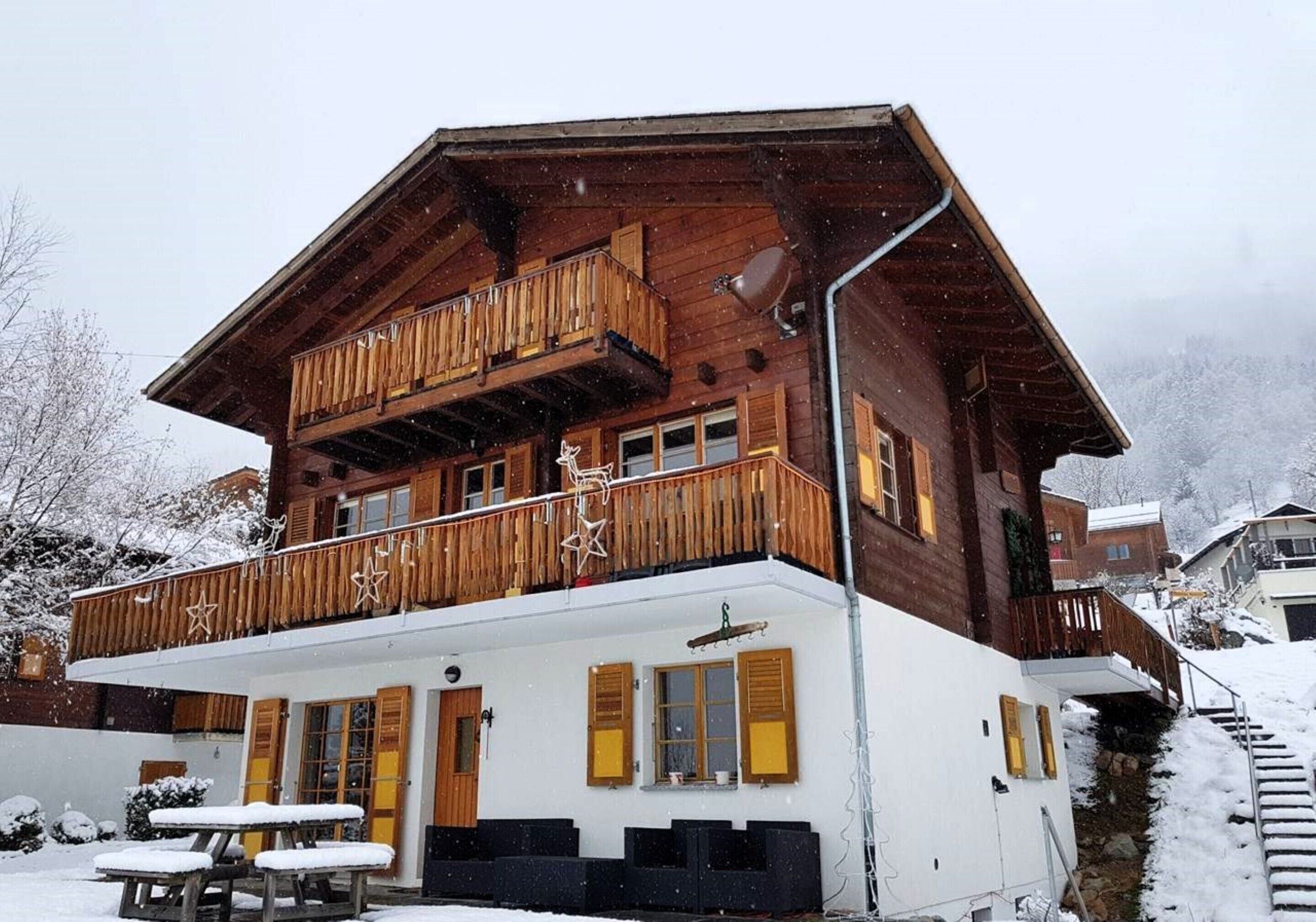 Een houten chalet met balkon, een overdekt terras en een trap naar de ingang.