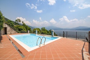 A swimming pool with steps leading down to a terrace, surrounded by a fence and overlooking a mountainous landscape.