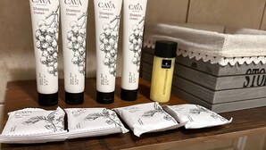 A bathroom counter with CAVA shampoo and conditioner tubes, a bottle of bresca conditioner, and a stack of towels.