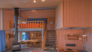 A cozy cabin interior with a wooden interior, a dining area, a sofa, a table, and a staircase leading to an upper level. - Perfektes Ferienhaus fur Familien (Rechlin)