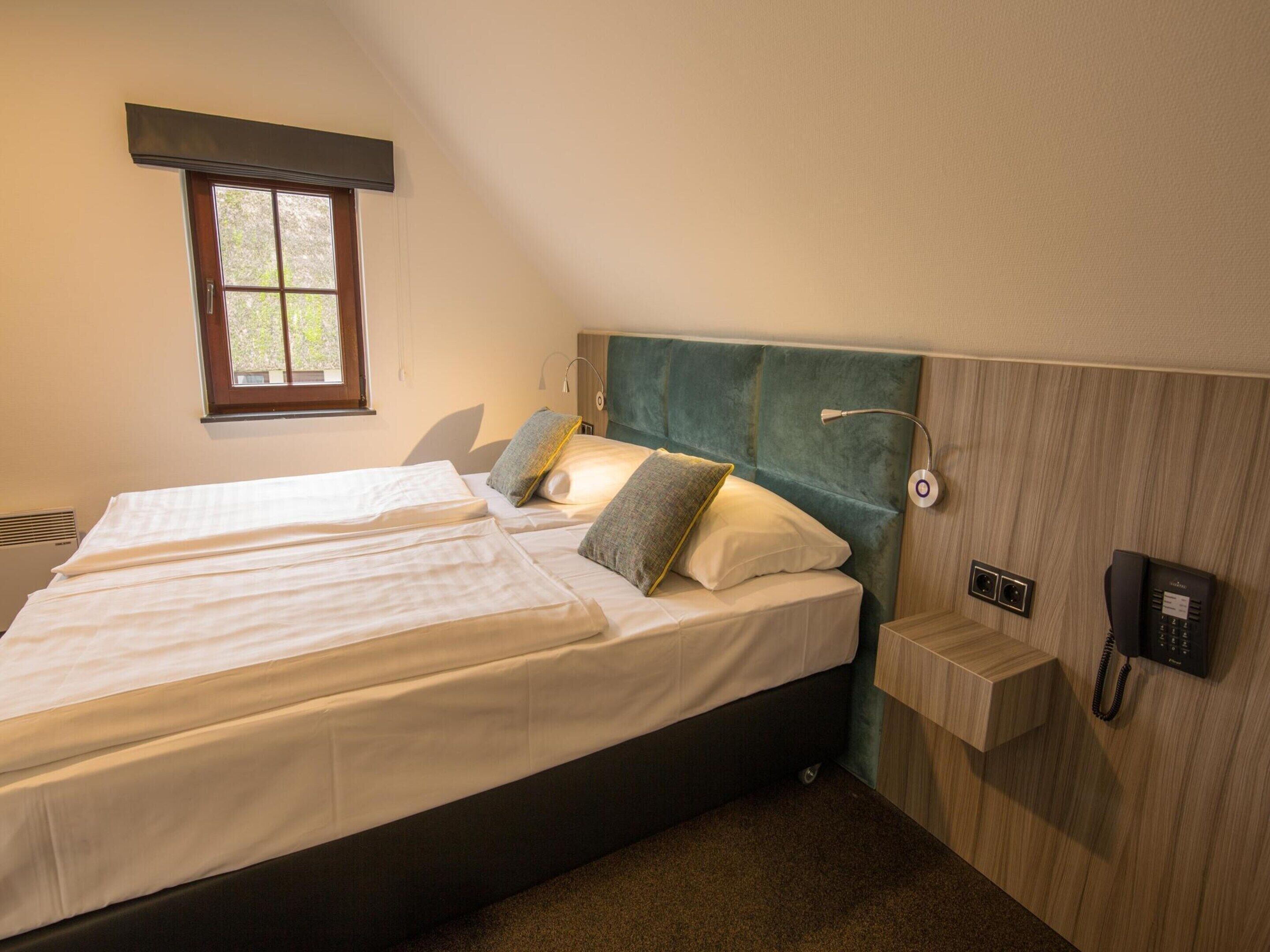 Un dormitorio con dos camas, una ventana, un teléfono en la mesita de noche y una lámpara de pared.
