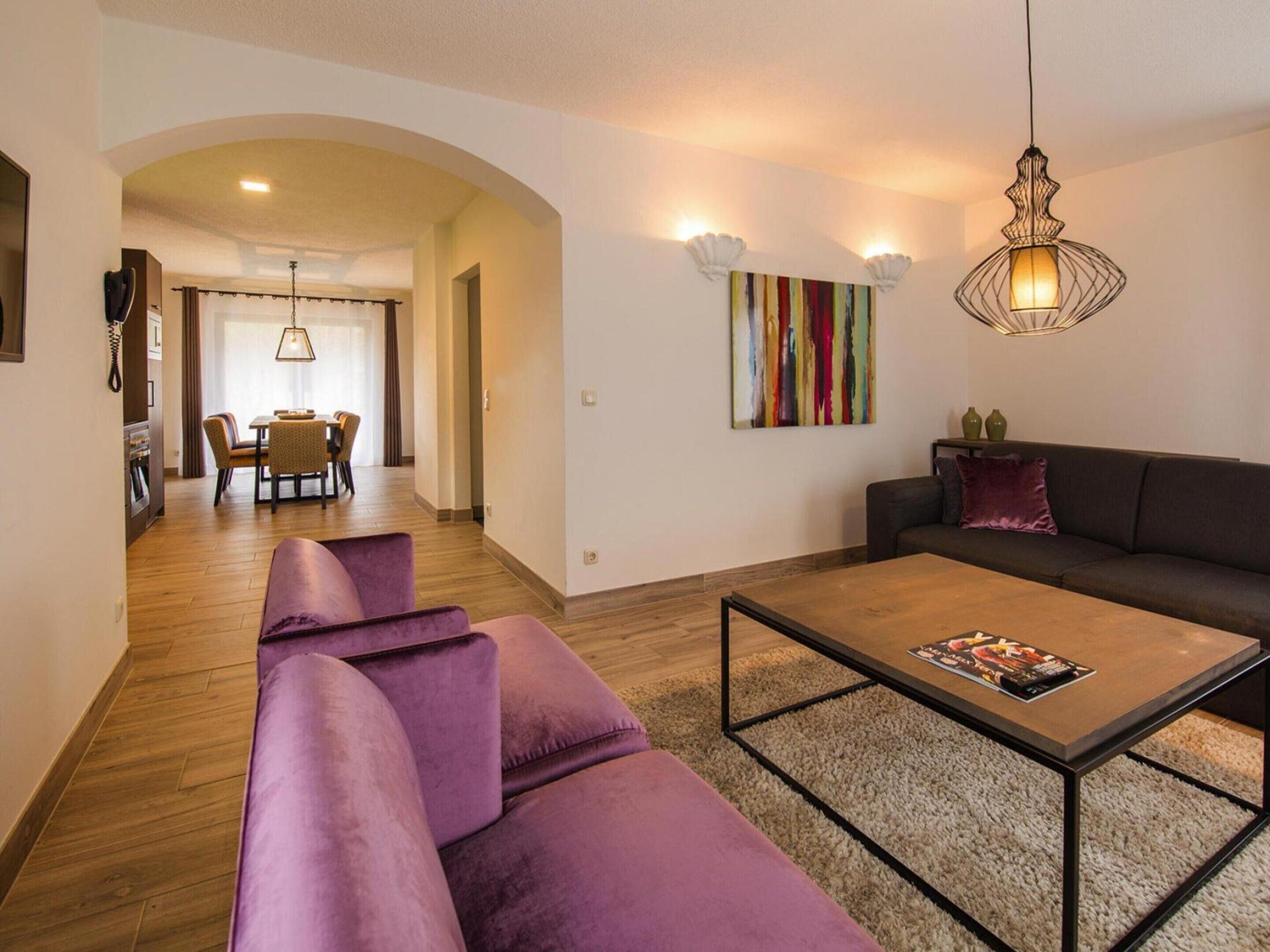 A modern living room with a sofa, a coffee table, and a dining area in the background.