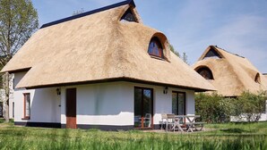 Ein Haus mit strohgedecktem Dach und weißer Fassade, ein Essbereich mit Außenbestuhlung und einem wolkenlosen Himmel.