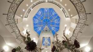 Ein prachtvoller Saal mit einem zentralen Chandelier, einem geometrischen Deckenmuster und dekorativer Eisenarbeit.