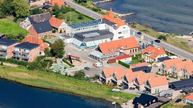 En vy från ovan av ett hotell vid kusten, med flera byggnader, en småbåtshamn och en väg som leder ner till stranden.