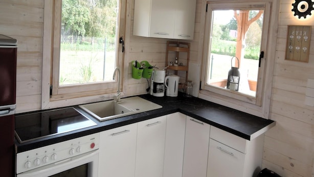 Cocina compacta con paredes de madera, encimera negra, armarios blancos y una ventana con vistas a zonas verdes.
