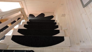 Una escalera de madera con escalones negros que ascienden, una barandilla de madera a la izquierda y un techo decorado con un engranaje.