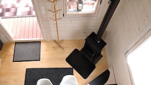 Un interior de madera con una estufa negra, una silla negra y un felpudo negro en el suelo.