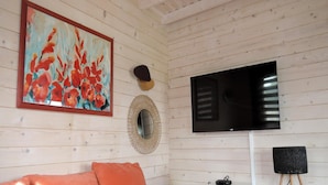 Un salón con decoración de madera, un televisor de pantalla plana grande montado en la pared, un espejo redondo y un cuadro enmarcado.