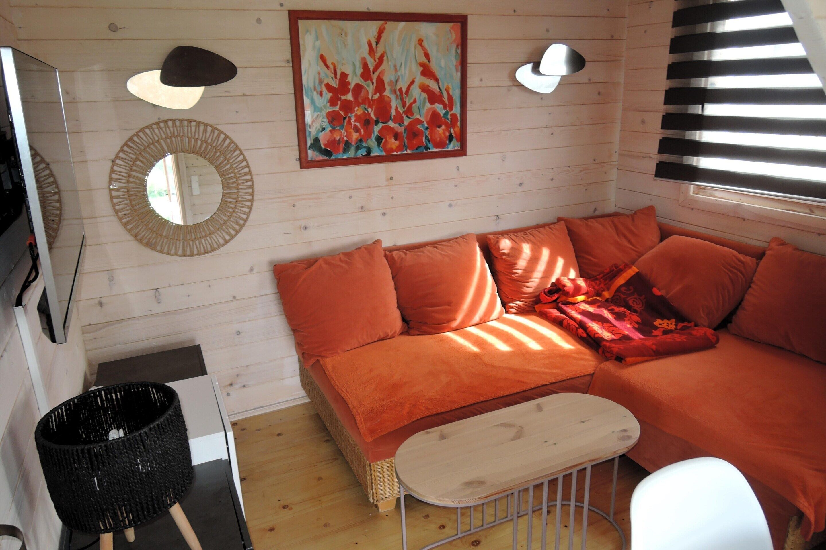 Een gezellige kamer met een grote oranje bank, een klein wit tafeltje, een rieten mand en een schilderij aan de muur.