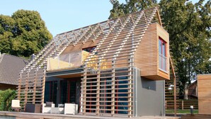 A modern house with a sloped roof, a wooden deck, and a large window. - Chalet in Wendorf (Kuhlen-Wendorf)