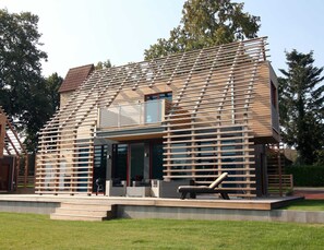 Una casa moderna con tetto spiovente, ampie finestre e un patio in legno.