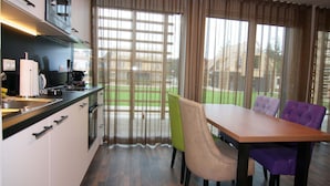 A modern kitchen with a dining area, featuring a large window with curtains, a wooden dining table, and two chairs. - Chalet in Wendorf (Kuhlen-Wendorf)