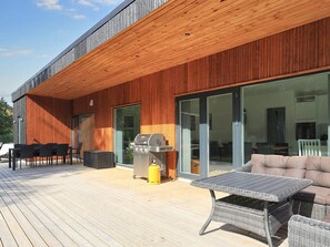 Eine moderne Terrasse im Freien mit Holzboden, Grill, Tisch und einer Couch.