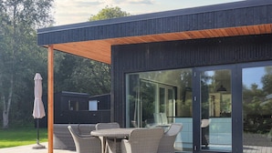 A modern outdoor patio with wicker furniture and a glass door leading to a room. - 12 Person Holiday Home in Vaeggerlose (Vaeggerlose)