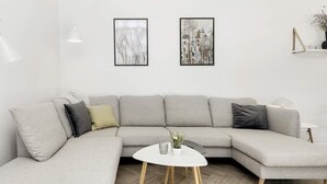 A modern living room with a grey sectional sofa, a small white round table, and two framed artworks on the wall. - 12 Person Holiday Home in Vaeggerlose (Vaeggerlose)