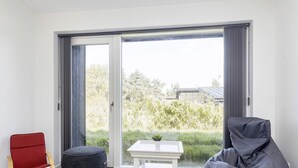 A modern living room with a sliding glass door leading to a garden, a red chair, a grey bean bag, and a small white table. - 12 Person Holiday Home in Vaeggerlose (Vaeggerlose)