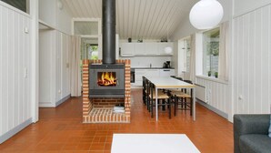 Et moderne køkken med en central murstensovn, hvide skabe og et spiseområde med bord og stole.