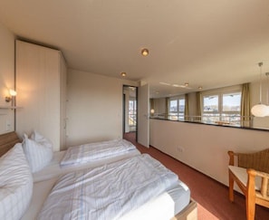 A hotel room with two beds, a sitting area with a chair, a large window with a view, and a mirror above the bed. - Ferienwohnung im Ferienpark Mueritz (Rechlin)