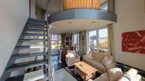 A modern living room with a curved staircase, a sofa set, and a large window with a view. - Ferienwohnung im Ferienpark Mueritz (Rechlin)