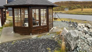 A wooden gazebo with a sloped roof, large windows, and a swing seat by a rocky shore. - 6 Person Holiday Home in Storslett (Nordreisa)