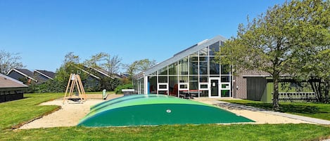 A modern building with a glass facade, a green play area, and a swing set.