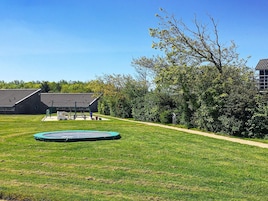 Un espacio al aire libre con césped, un trampolín, un edificio con techo inclinado y un sendero que conduce a él.
