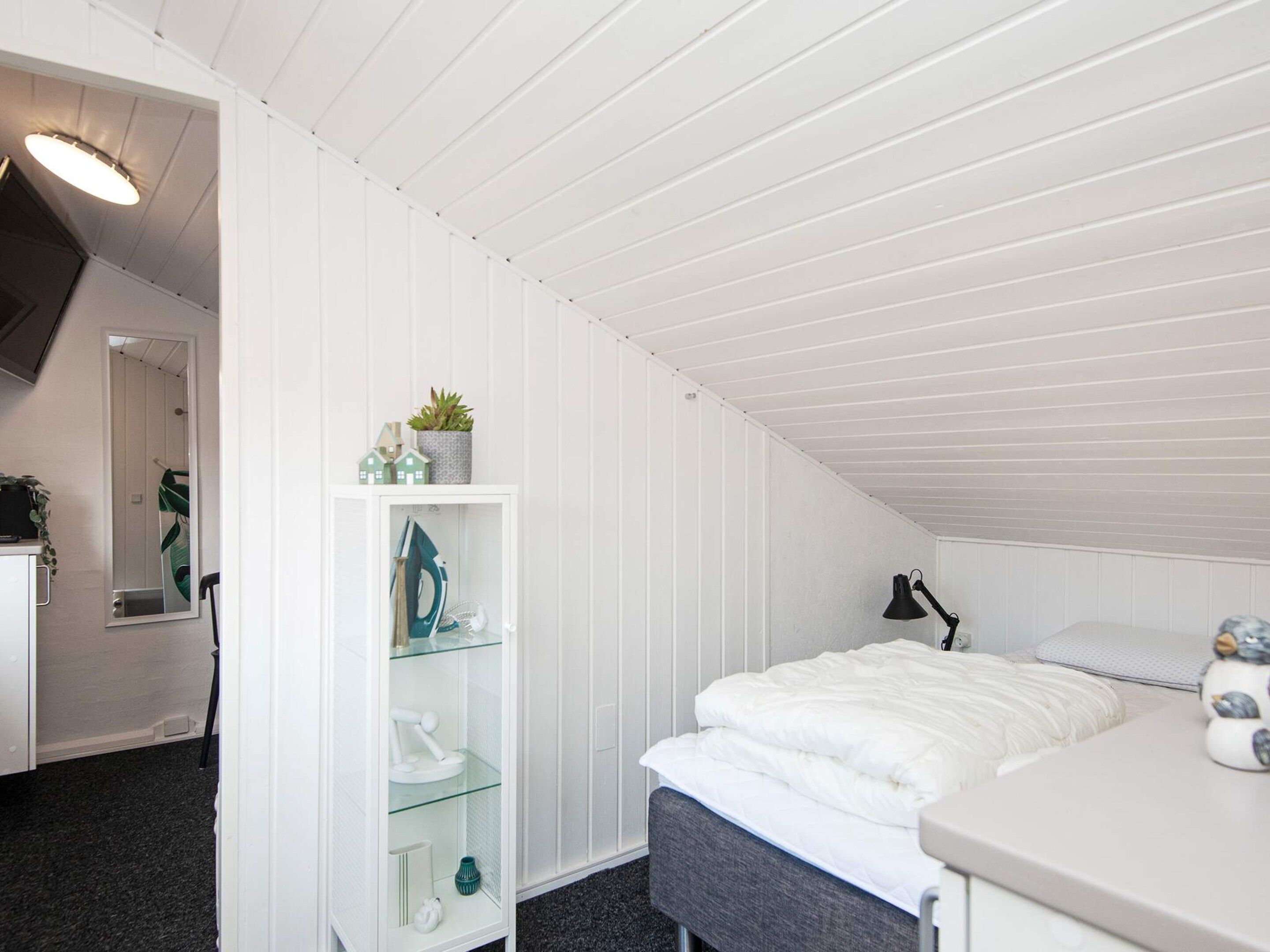 A bedroom with a sloped ceiling, a bed, a desk, and a shelving unit with decorative items.