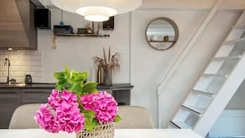 A modern kitchen with a white ceiling light, a dining table with a woven basket of pink flowers, and a staircase with a white railing.