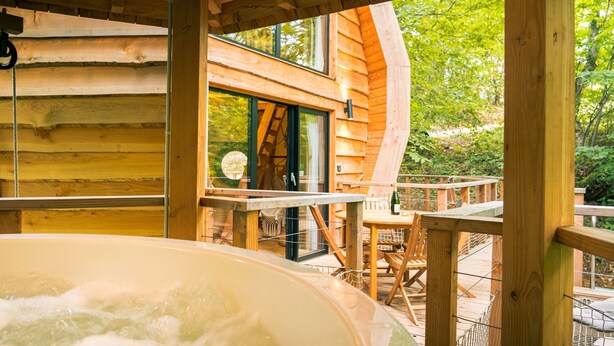Una baita in legno con vasca idromassaggio, terrazza in legno e vista sulla foresta circostante.