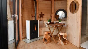 Accogliente interno di una baita in legno con camino, uno specchio tondo e un tavolino con una pianta e una bottiglia.
