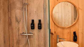 A wooden-paneled bathroom with a shower, a sink, and a round mirror.