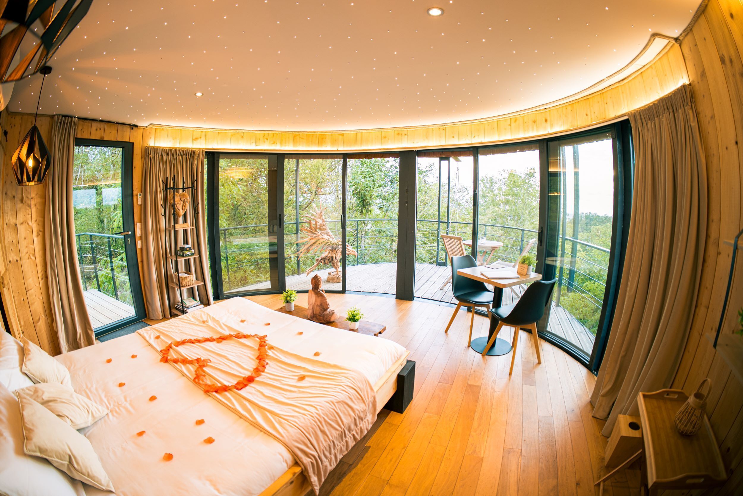 Un dormitorio con una cama grande, una mesita y una silla. Tiene un balcón con barandilla y vistas al verdor.