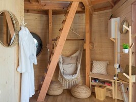 A wooden cabin interior with a hammock chair, a white robe hanging, and a shelf with various items.