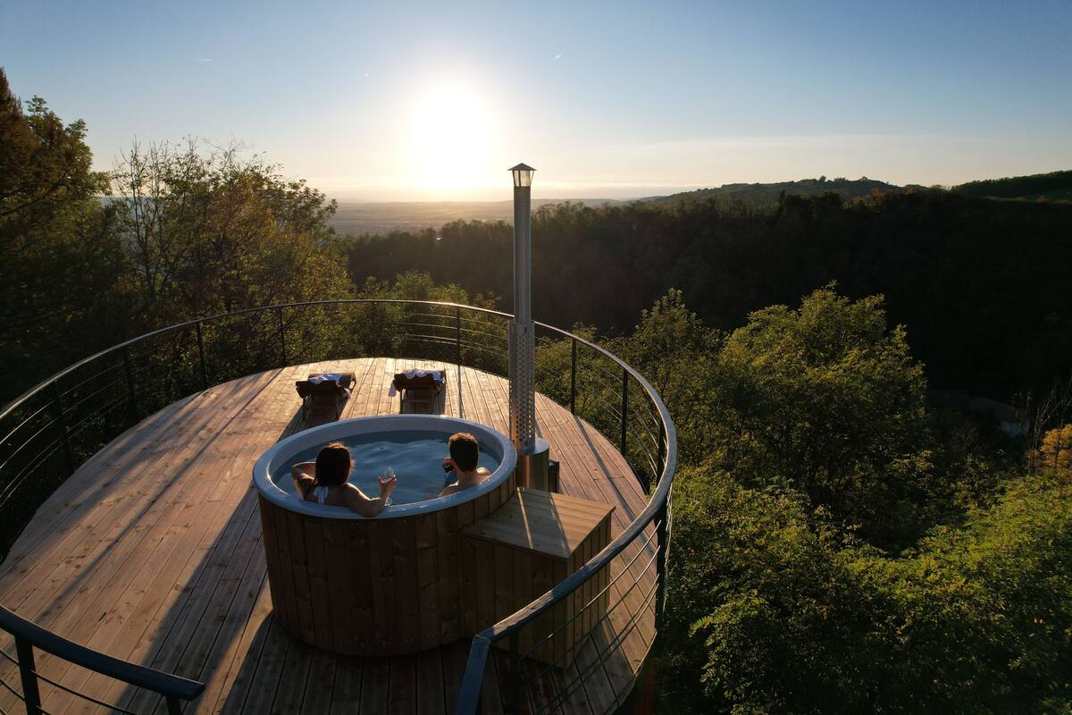 Um deck de madeira com hidromassagem e área de estar, rodeado por árvores e com vista para um vale.