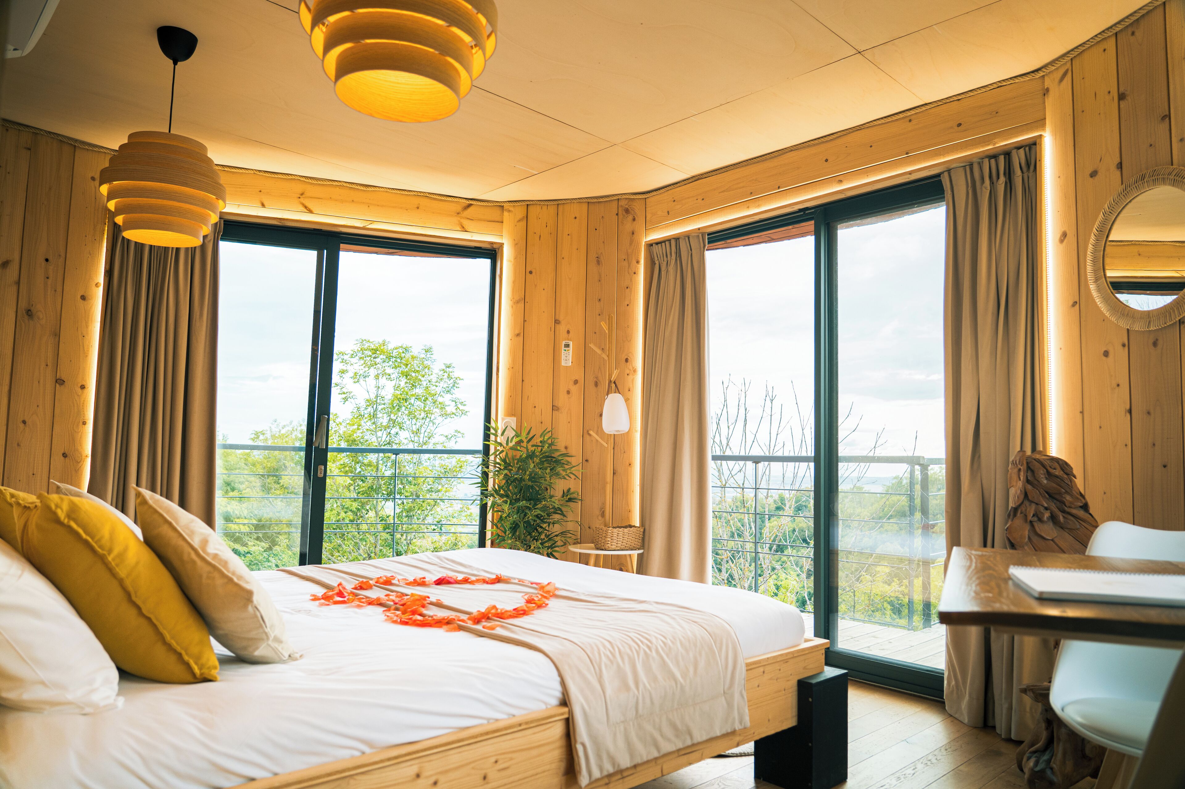 A wooden room with a bed, a desk, and large windows.