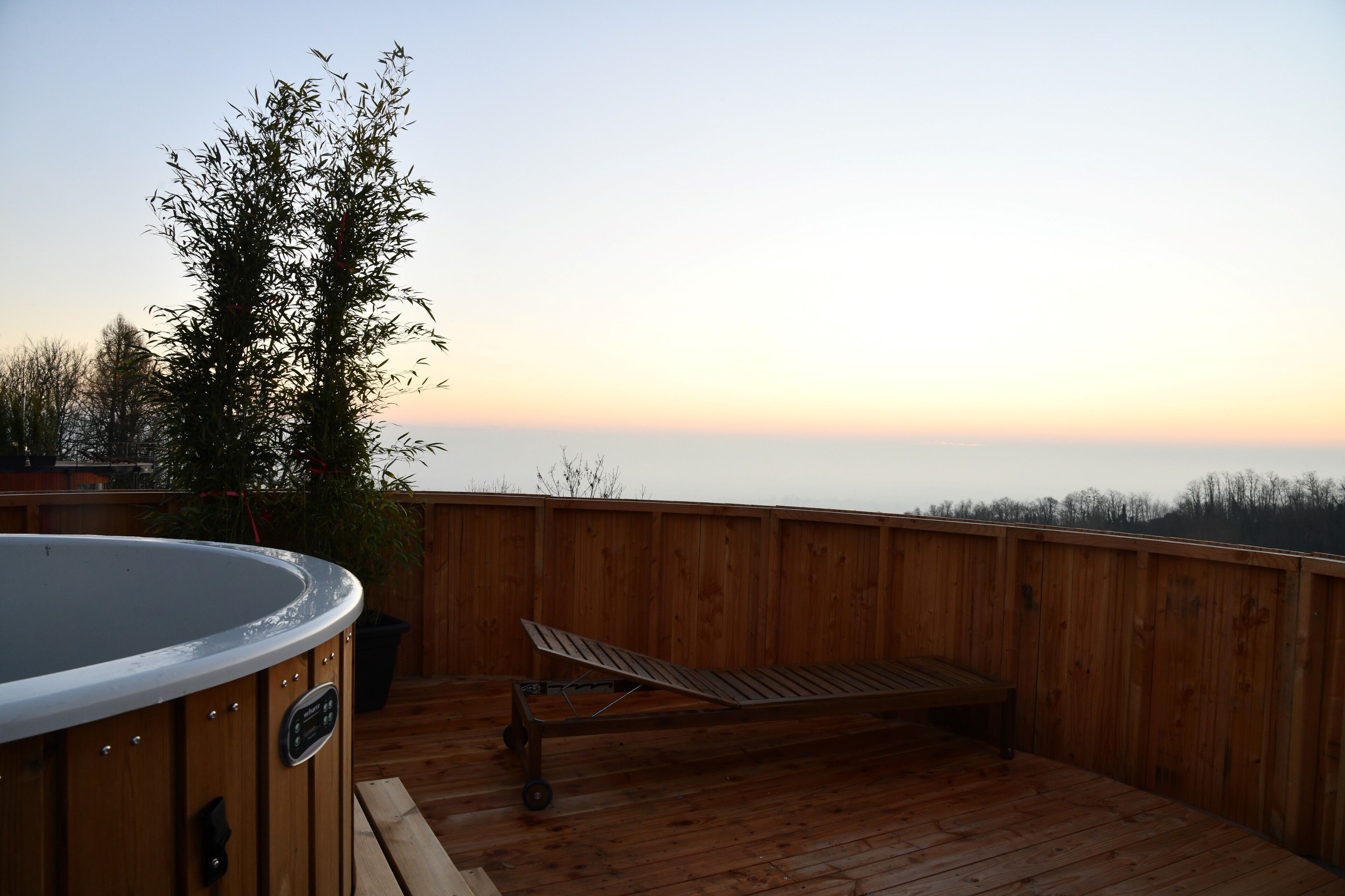 A wooden deck with a hot tub, lounge chair, and a wooden fence.