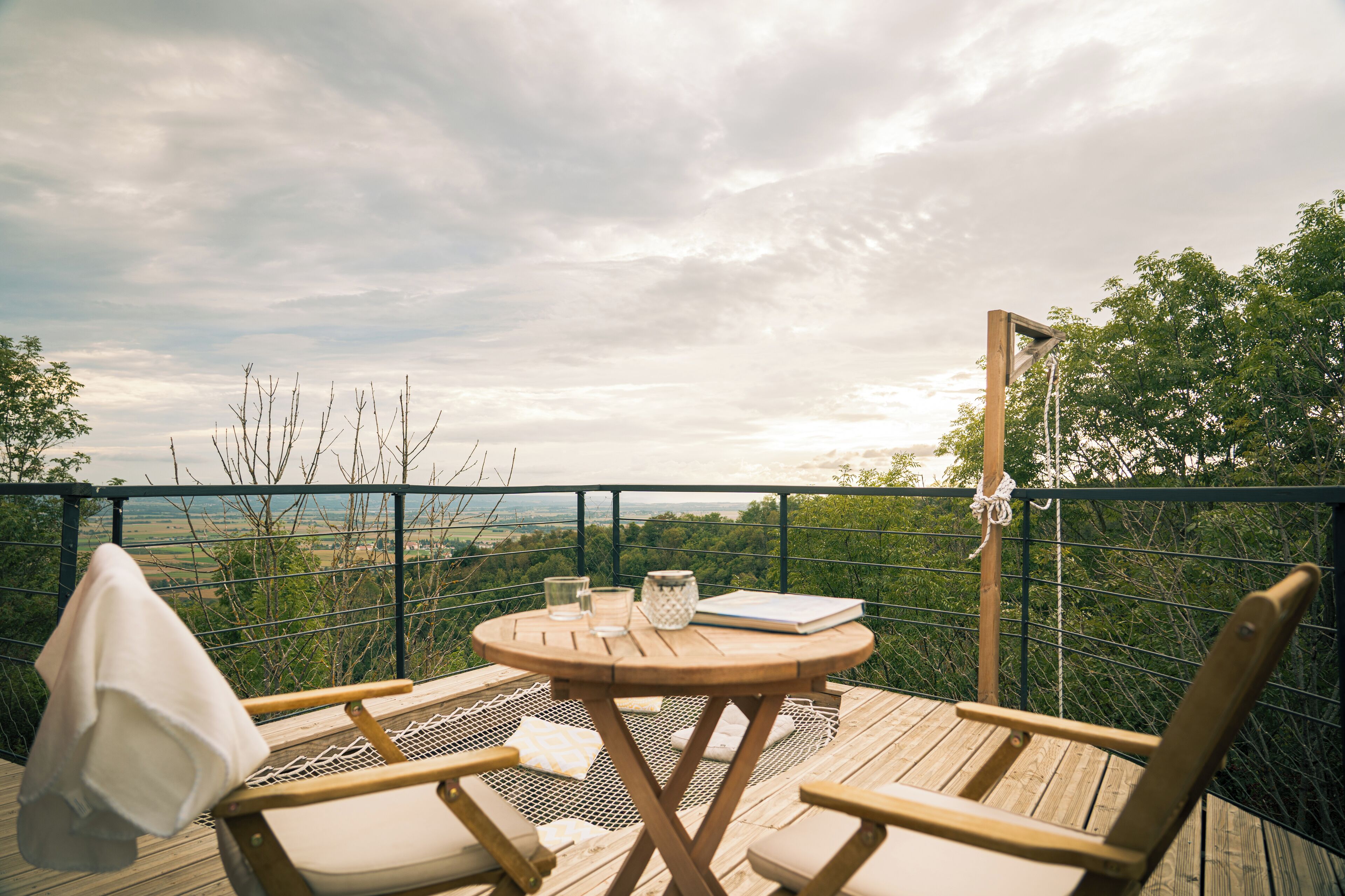 Una terraza de madera con una mesa redonda y dos sillas, una toalla y un libro.