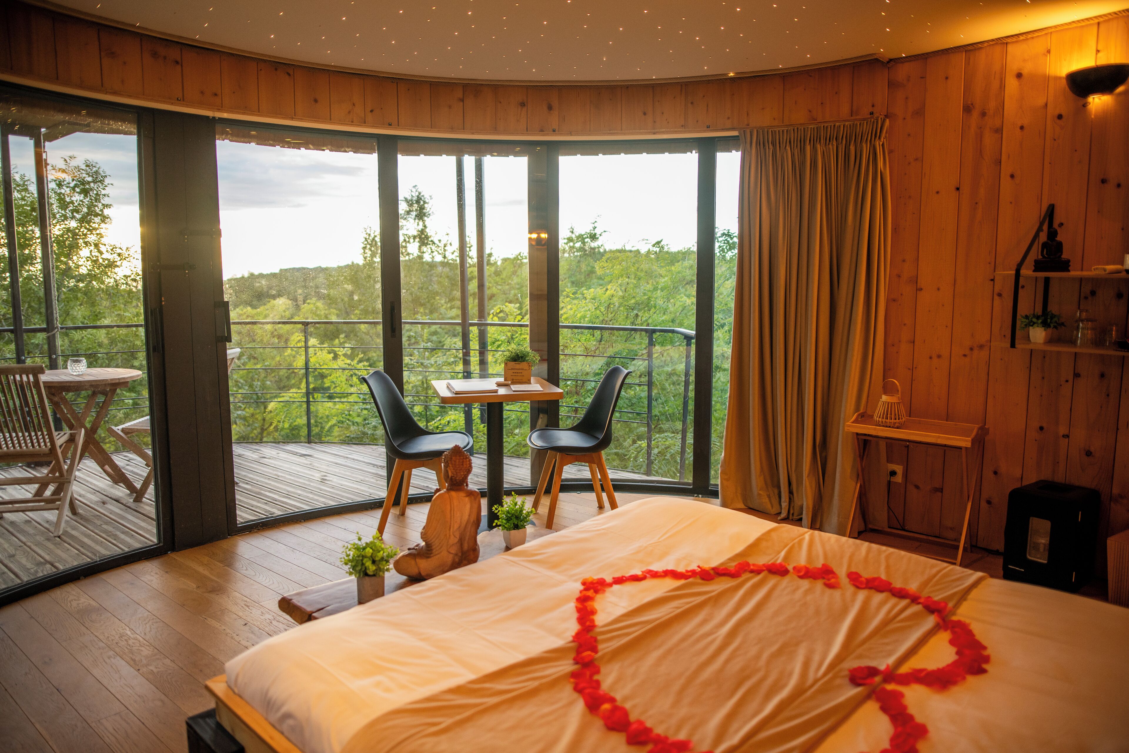 A bedroom with a large bed, a view of the outdoors, a small table, and two chairs.