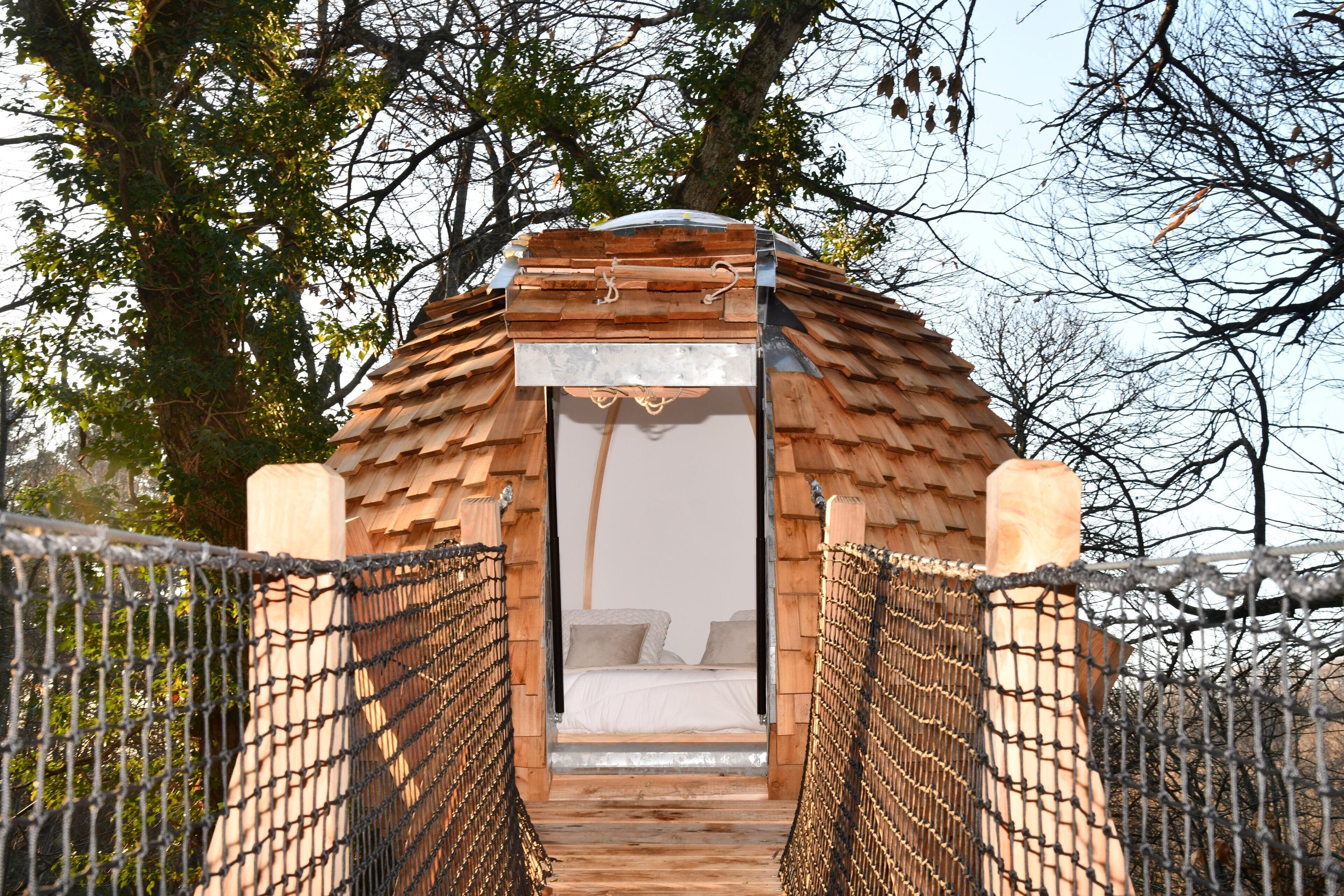A wooden bridge leading to a small, enclosed room with a bed and a window.