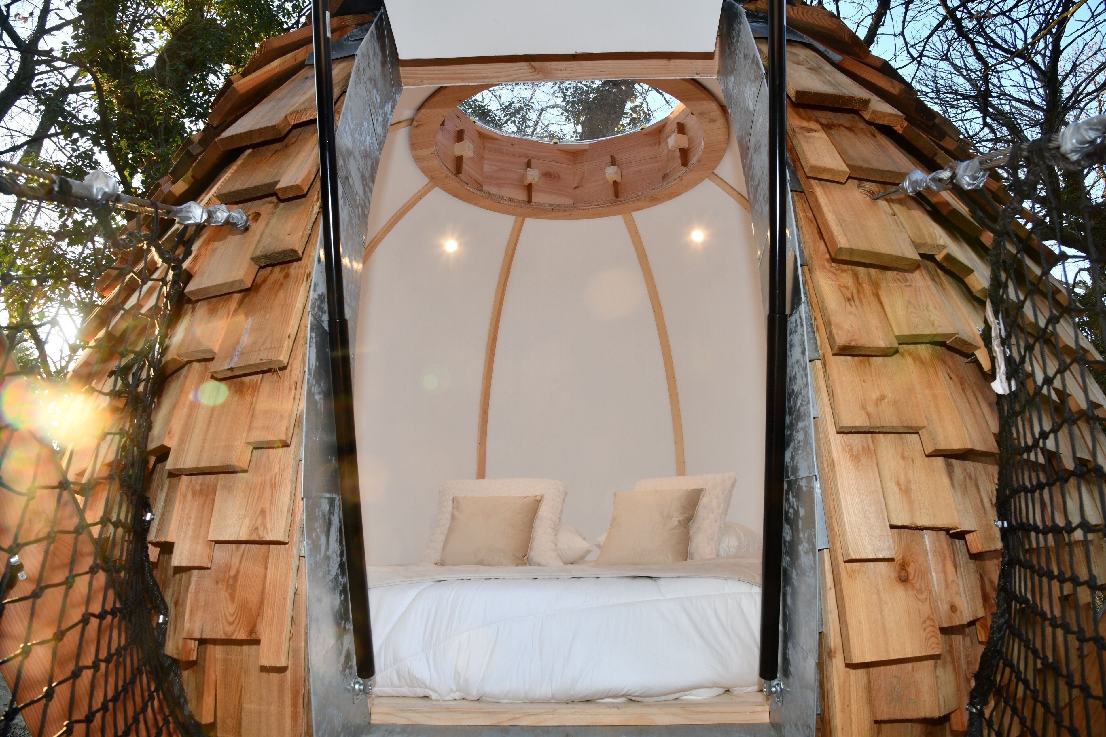 Estructura circular de cama de madera con dosel, rodeada de árboles.