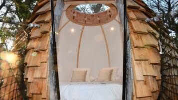 Estructura circular de cama de madera con dosel, rodeada de árboles.