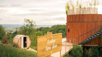 A wooden sign reading "Lodge Spa Zen" with a wooden barrel and a wooden structure in the background.
