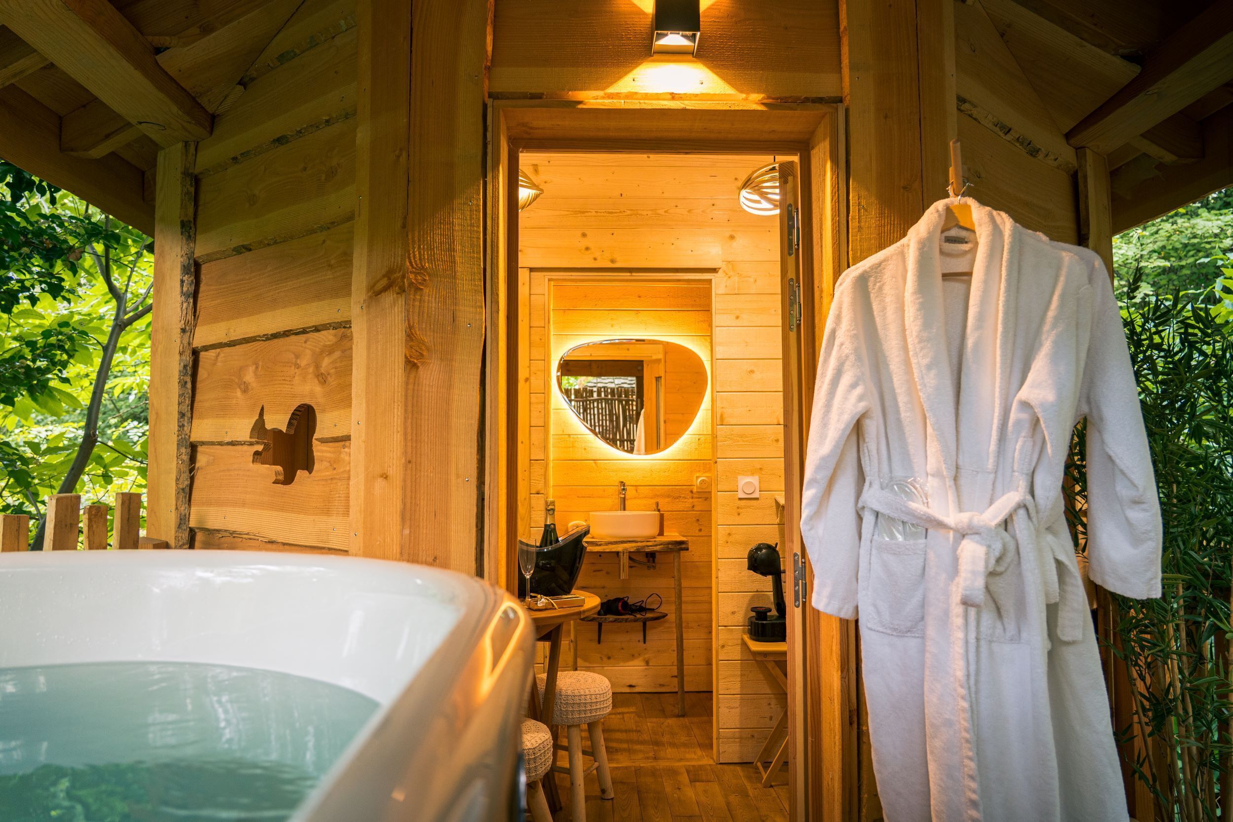 Een houten chalet met een jacuzzi, een houten bankje en een badjas hangend aan een rek.